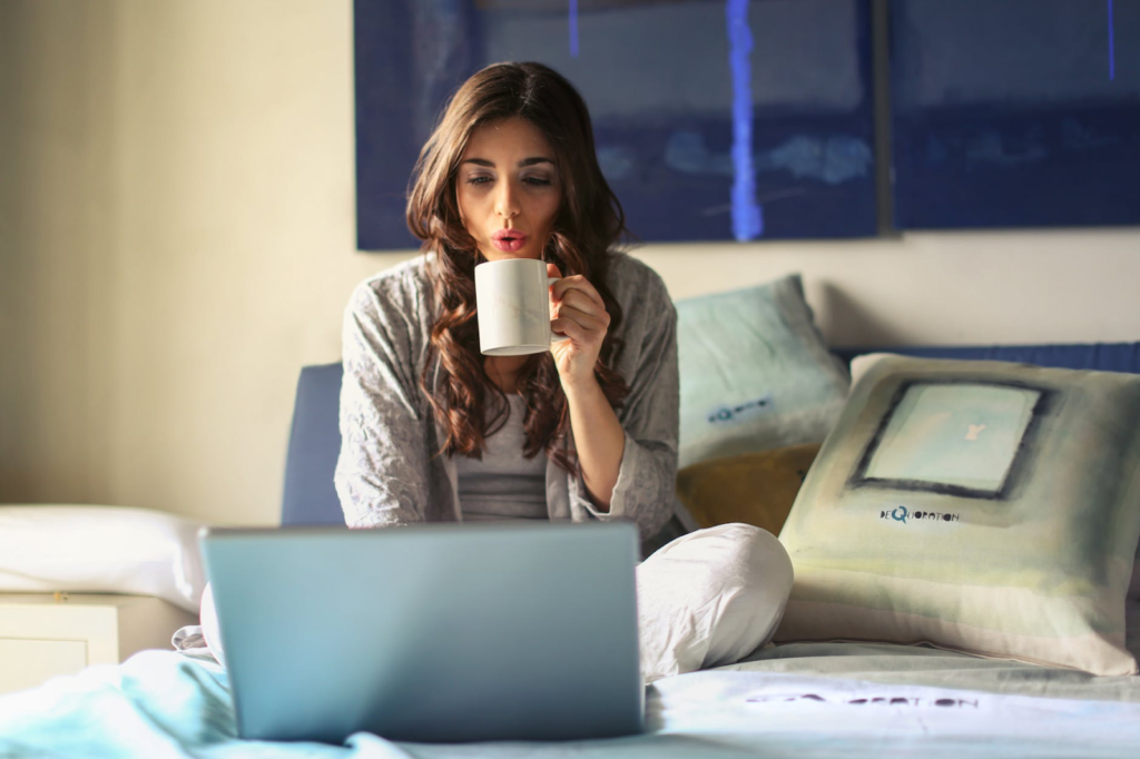 women relaxing on bed with a laptop and holding a hot mug
