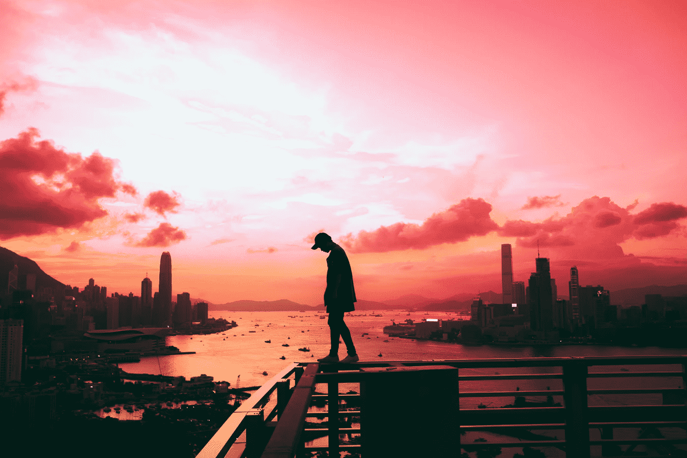 Silhouette of person standing on railing against pink sunset