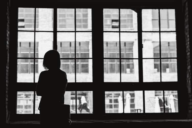 Woman alone staring out a window in black and white