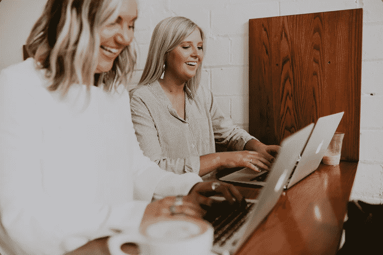 Two women type on their laptops and smile as an example of personal connection with technology.