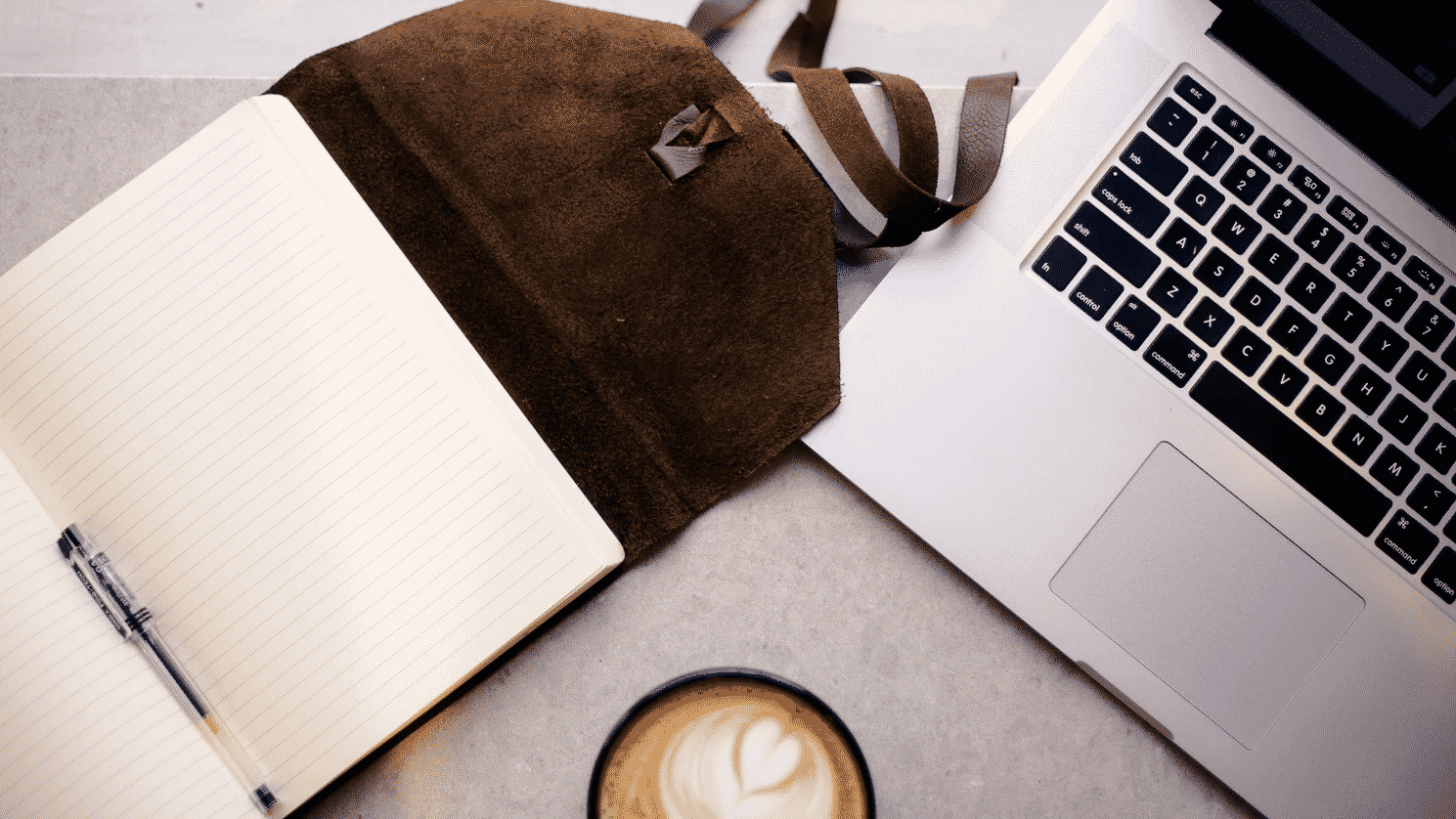 Laptop next to notebook and coffee